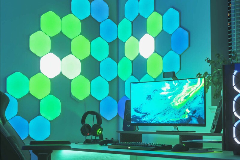 Nanoleaf Shapes Hexagon LED lights shining green in next to a computer on a wall.