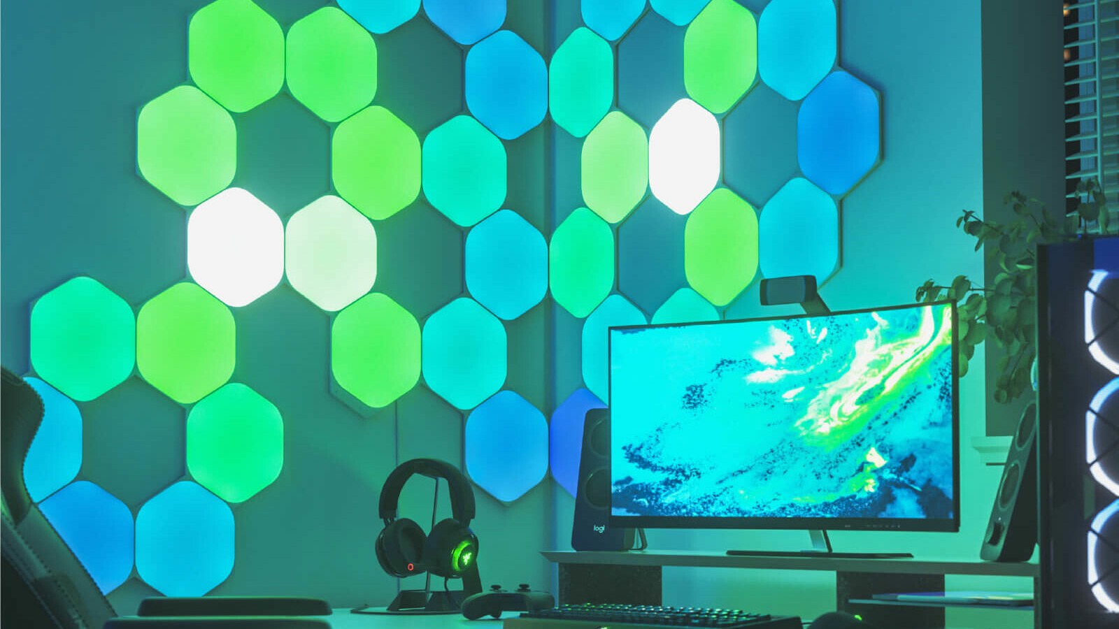 Nanoleaf Shapes Hexagon LED lights shining green in next to a computer on a wall.